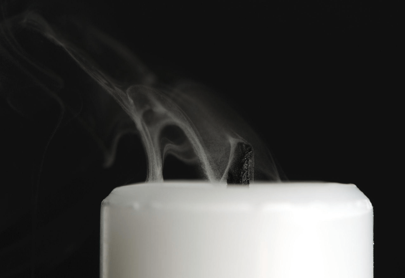 Close-up of a white candle with smoke rising from the black wick against a black background.