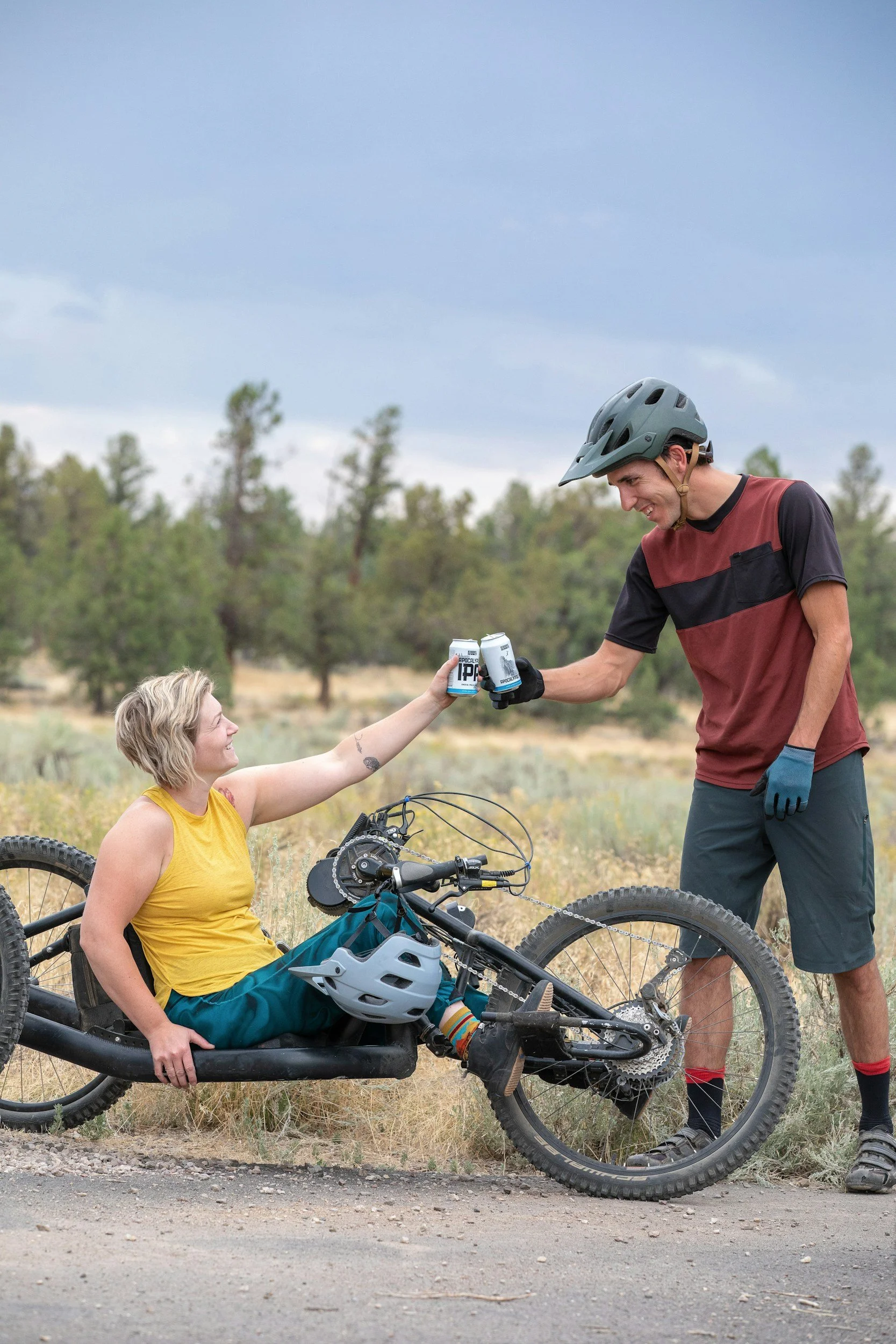 person in a hand cycling clinking soda cans with a standing cyclist