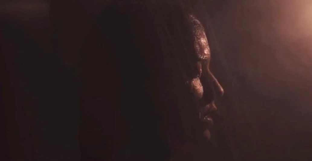 A dark image showing a close-up side profile of a person's face illuminated by a soft, warm light.