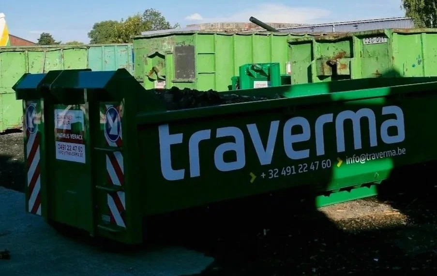 A green dumpster with white and blue lettering reading 'Traverma' and contact information, situated outdoors with other containers and trees in the background.