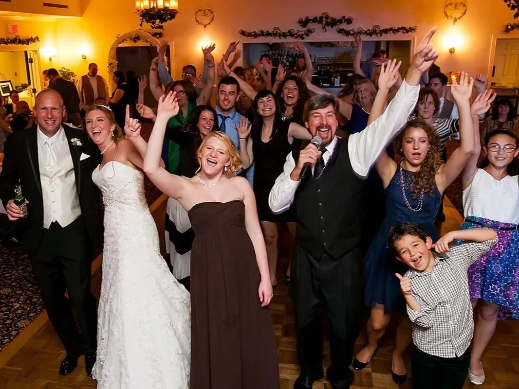 Celebrating wedding reception with bride, groom, family, and friends dancing and smiling at a decorated reception hall.