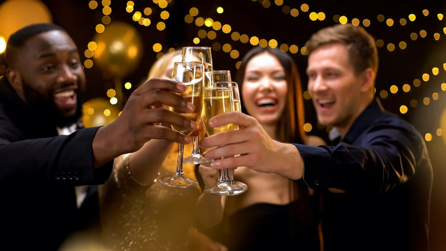 Group of friends in formal attire celebrating with toasts at a party, with warm lighting and decorated background.