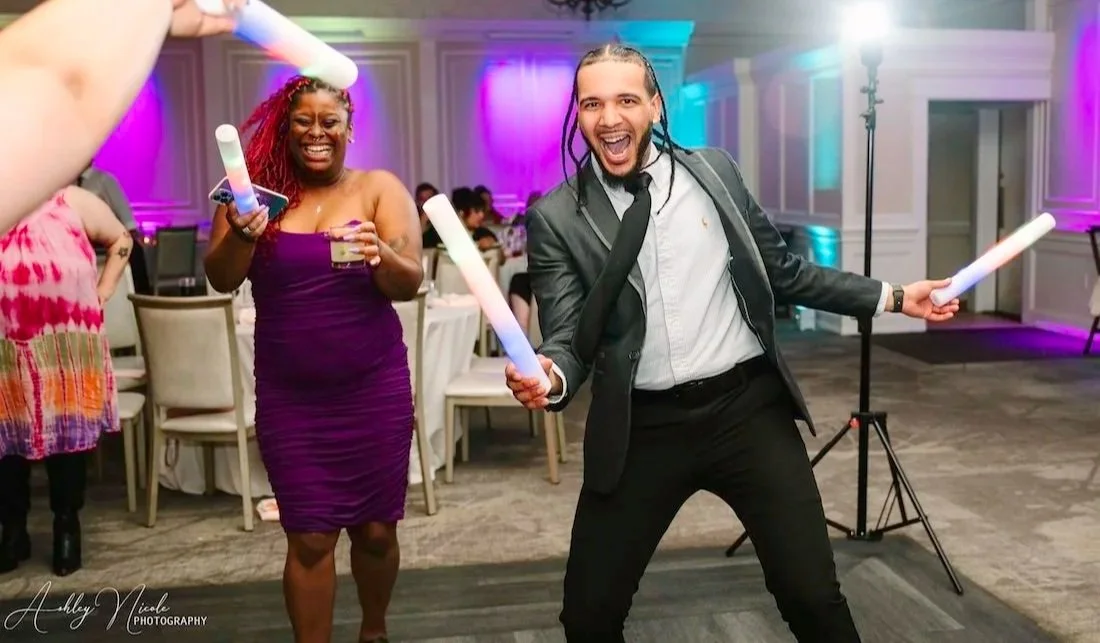 People celebrating at a party with glow sticks, with purple and blue lighting, in a decorated banquet hall.