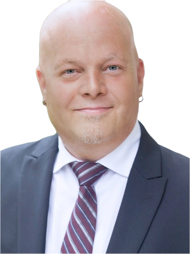 A bald man with a light complexion and a goatee, wearing a dark suit, white dress shirt, and a striped tie, smiling at the camera.