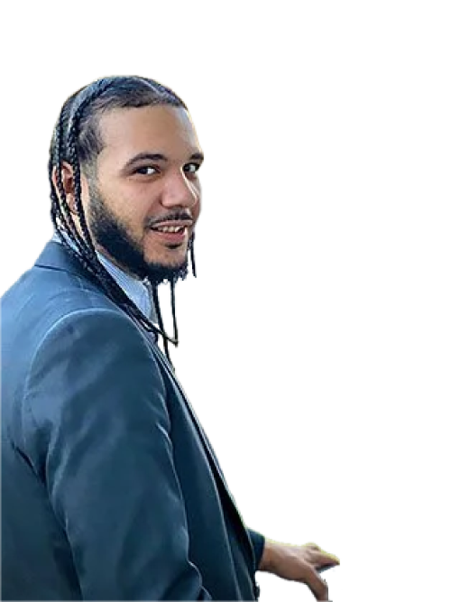 A man in a blue suit smiling and looking over his shoulder, with braided hair.