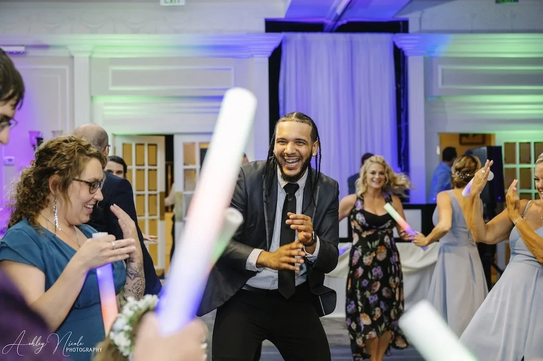 People dancing and laughing at a party with colorful lighting, holding glow sticks.