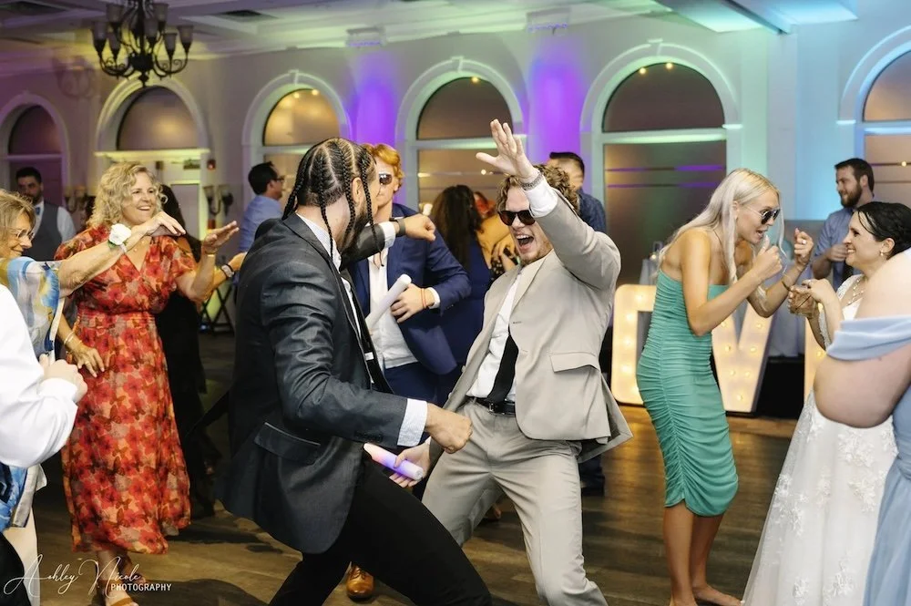 People dancing and having fun at a lively indoor party or celebration, with colorful lighting and smiling faces.