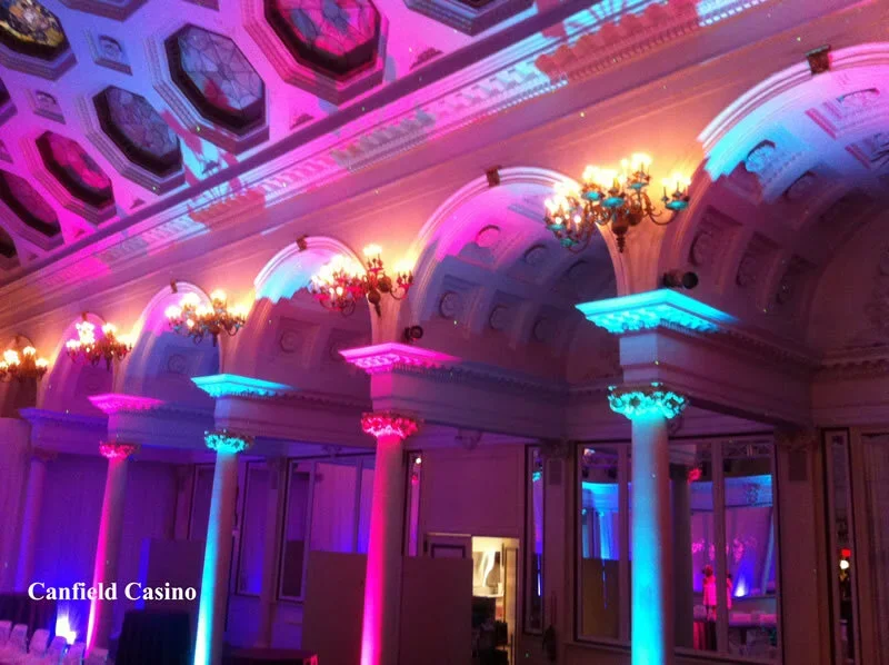 Interior view of Canfield Casino illuminated with colorful pink and blue lighting, featuring ornate columns, chandeliers, and a decorated ceiling.