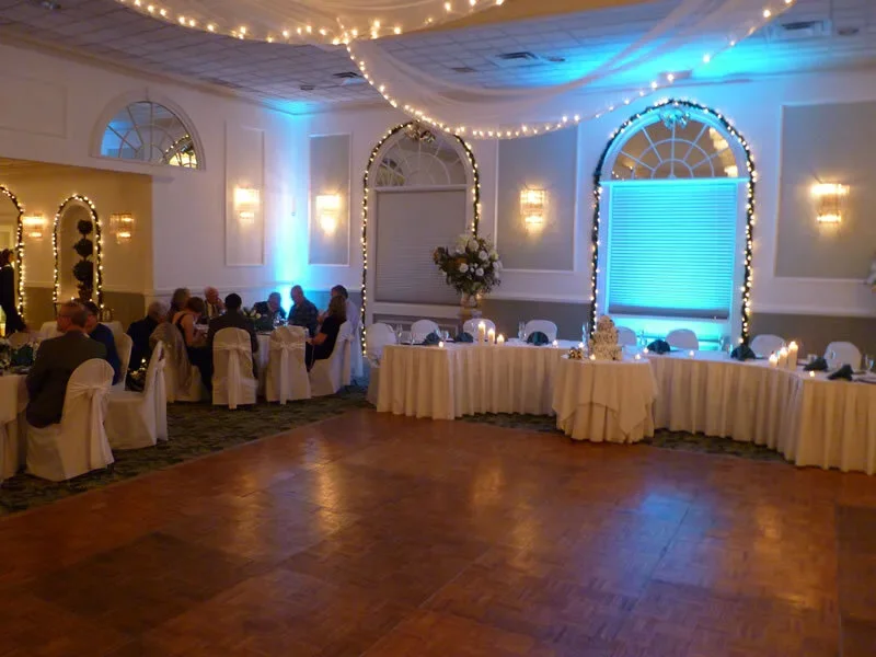 Indoor event space decorated with string lights, blue uplighting, and elegant table settings for a wedding reception or banquet.