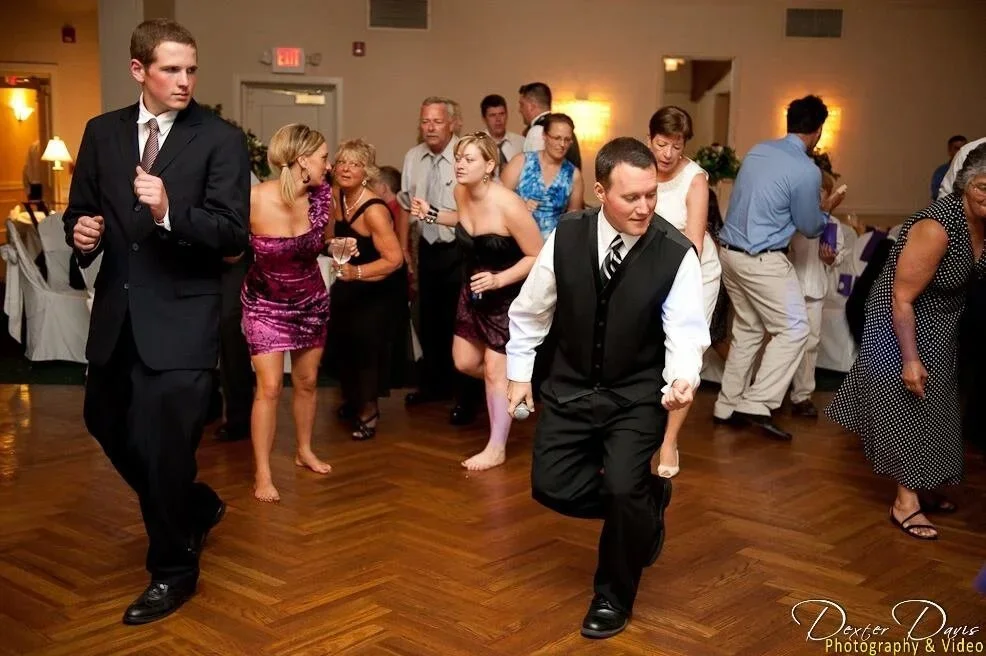 People dancing at a formal event in a banquet hall, with some dressed in suits and dresses.