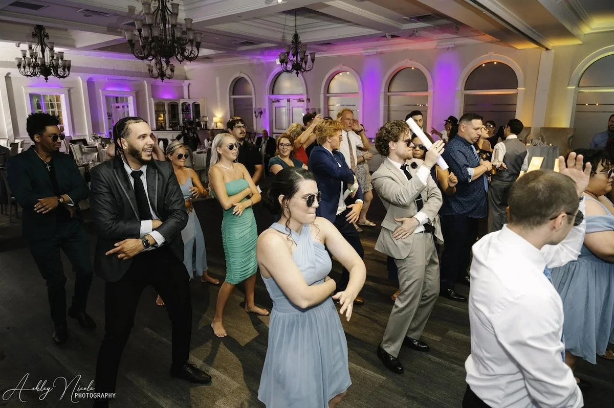 People wearing formal attire dancing at a wedding reception with purple and yellow uplighting in the background.