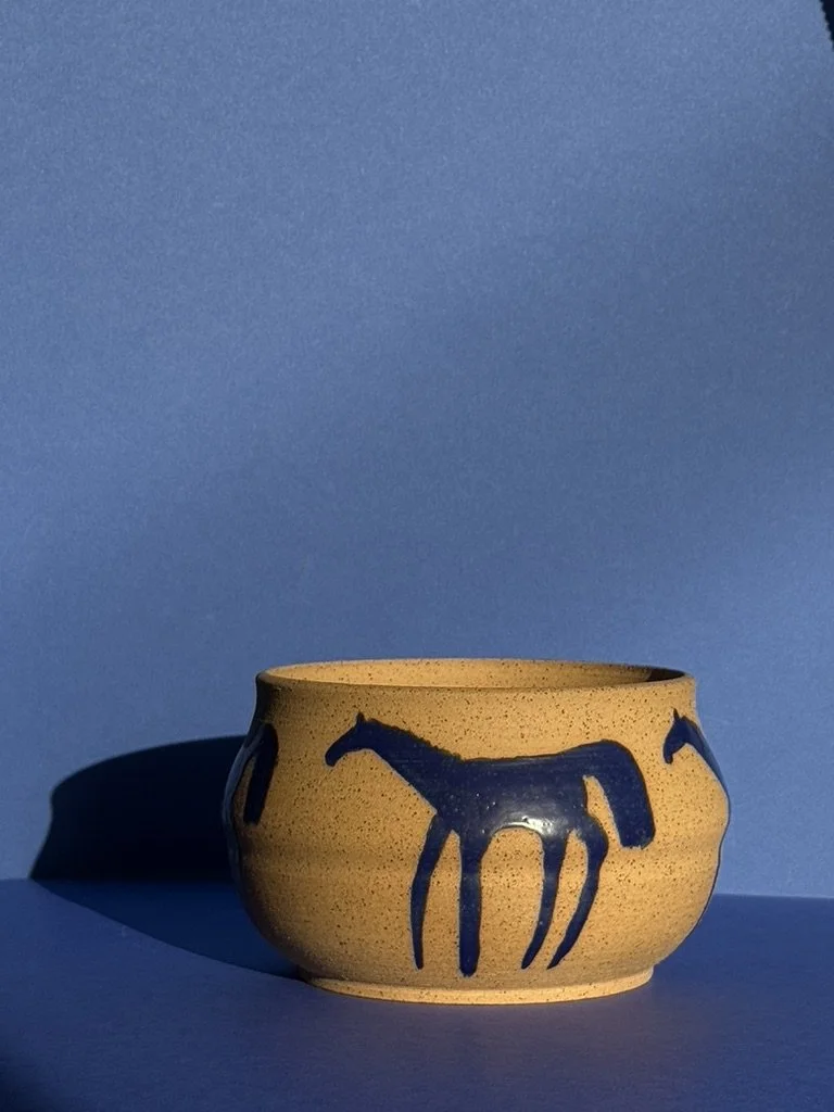 A beige ceramic bowl with blue horse illustrations on the side against a matching blue background.
