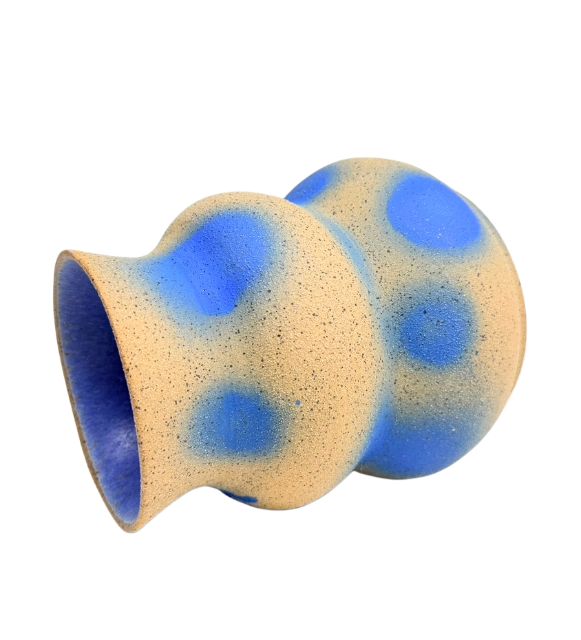 A beige ceramic vase with blue polka dots, rounded shape, and textured surface.