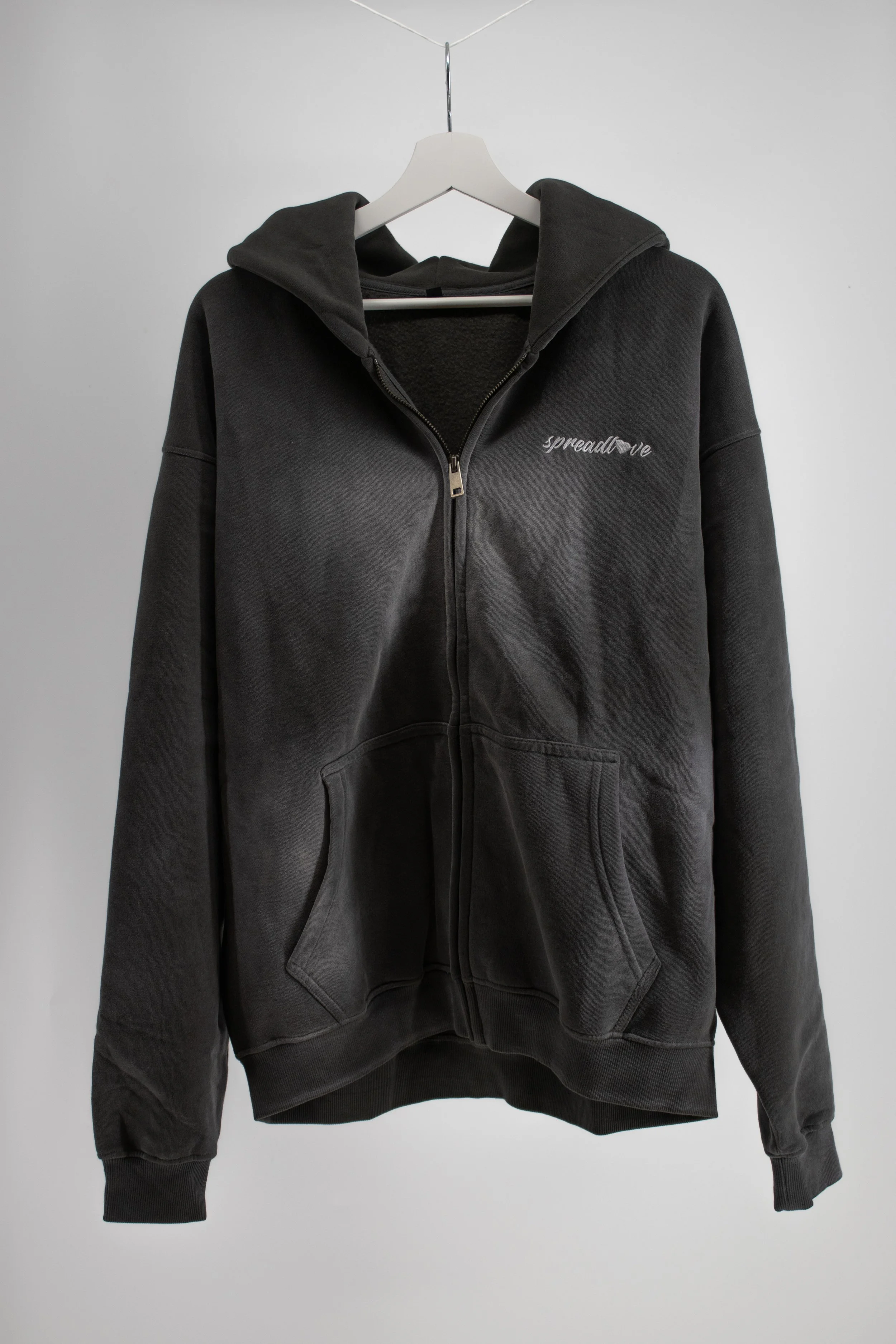 Veste à capuche noire suspendue sur un cintre contre un mur blanc.