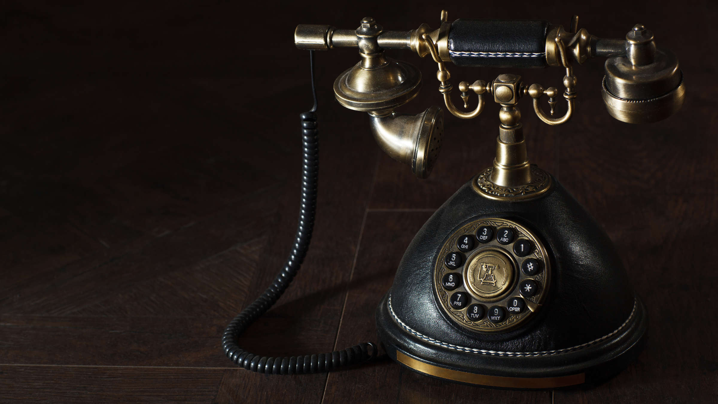 Vintage rotary telephone with brass and black finish on a dark wooden floor.