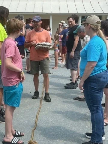 People gathered outside, with one man holding a turtle on a tray, surrounded by onlookers