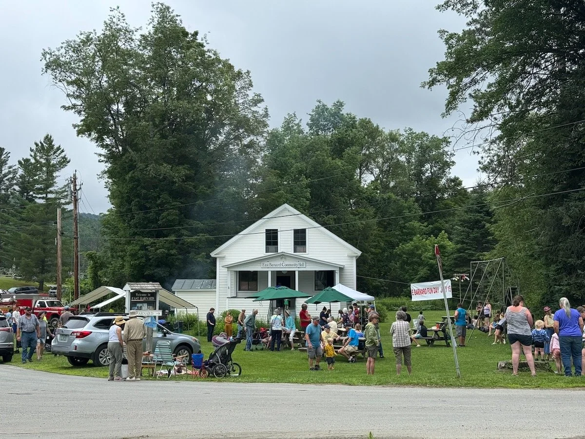 People gathered in front of East Barnard Community Hall during Barnard Fun Day with tents, umbrellas, and a playground.