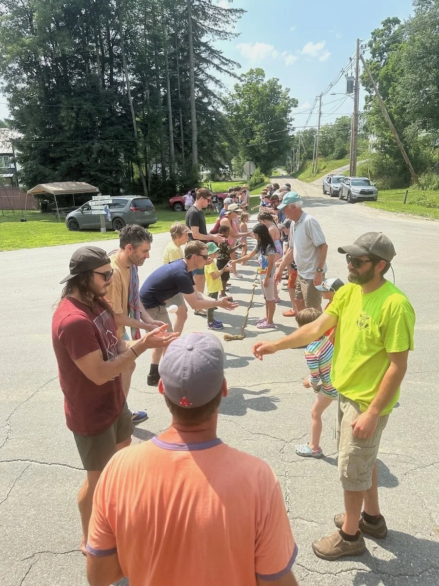 People participating in a tug-of-war game outdoors on a sunny day, standing in two lines holding a rope.