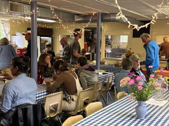 People dining in a cozy restaurant with checkered tablecloths, string lights, and flowers on the tables.