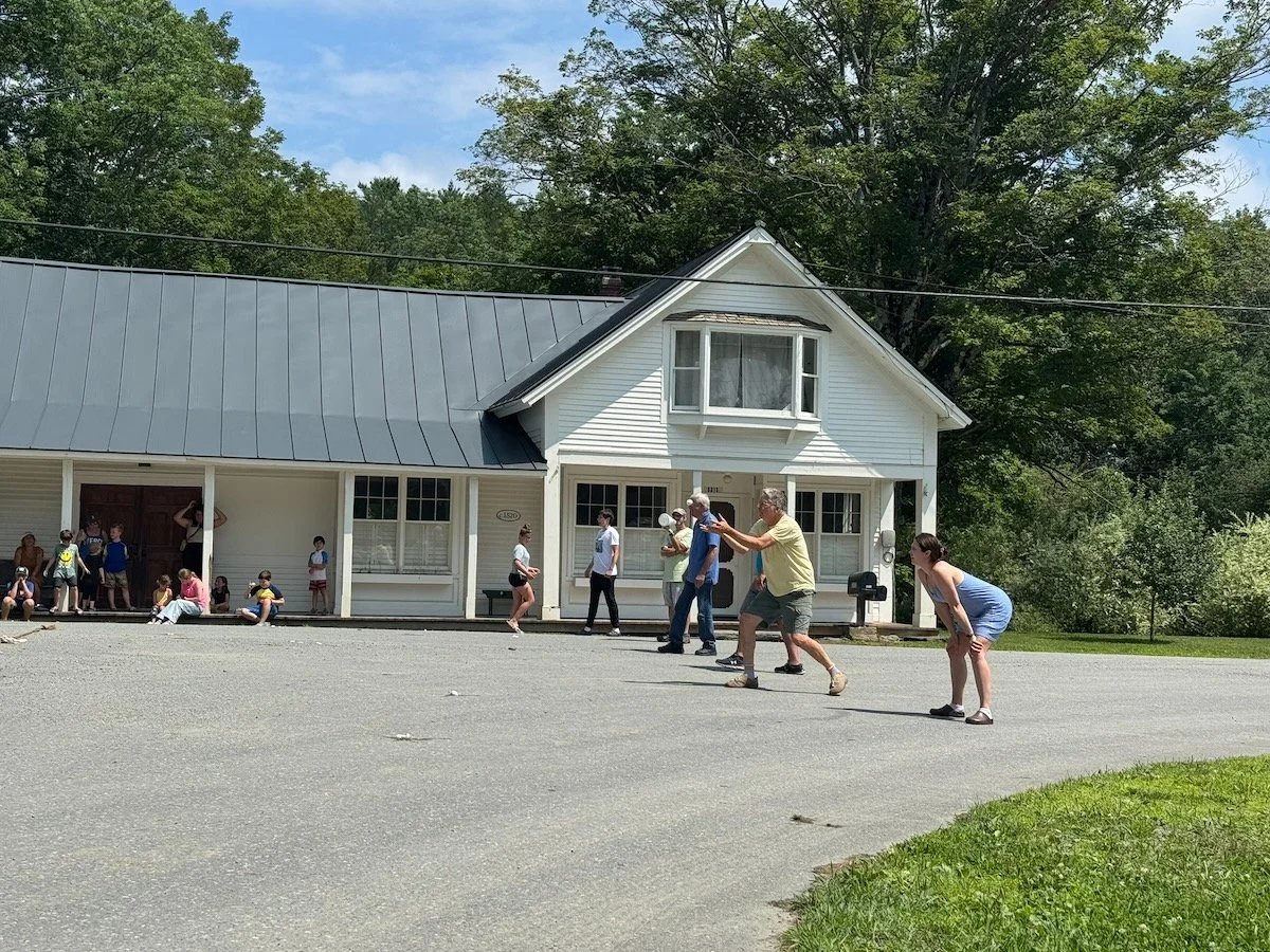 People playing a game outside a white house with a blue roof on a sunny day.