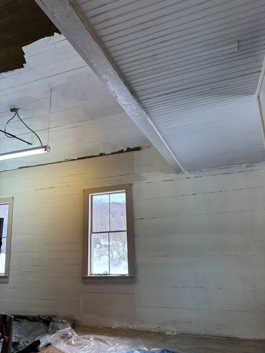 Interior of a room under construction with unfinished walls, ceiling, and exposed wiring, featuring a window showing a snowy landscape outside.
