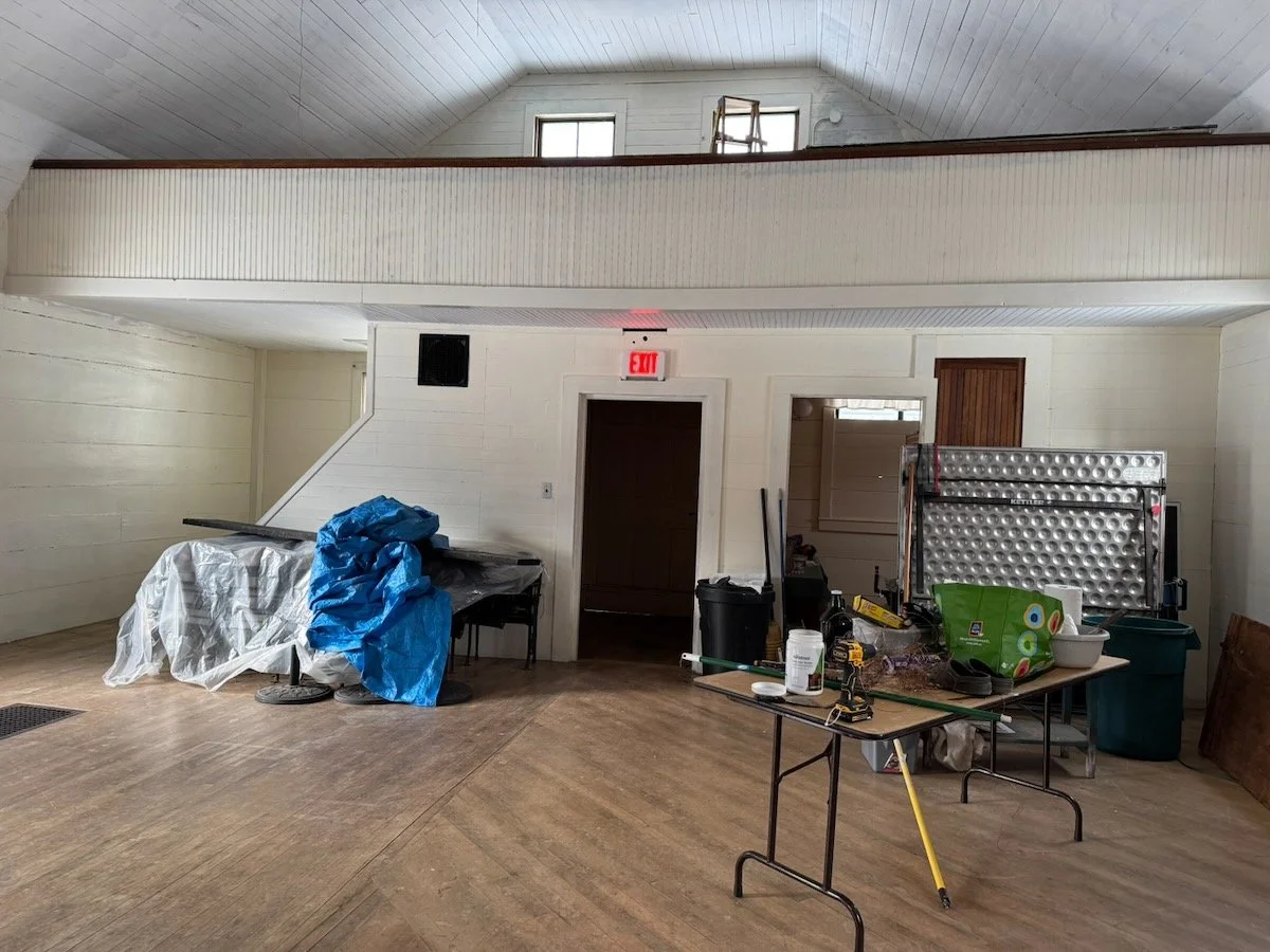 Indoor space with a high ceiling, table with tools and supplies, covered object, and a foldable metal event structure.