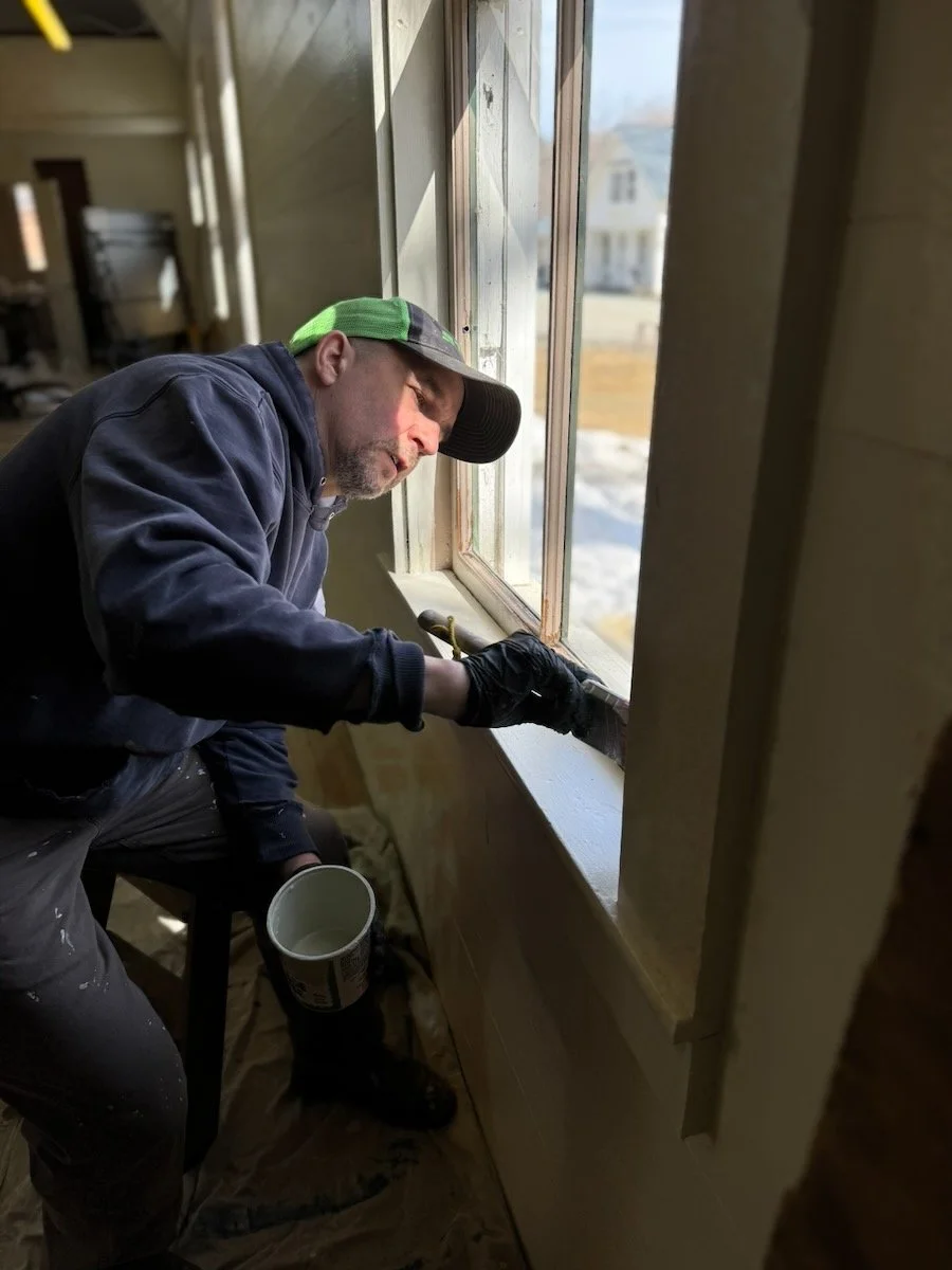 Man applying paint or sealant to window frame inside a house during construction or renovation.
