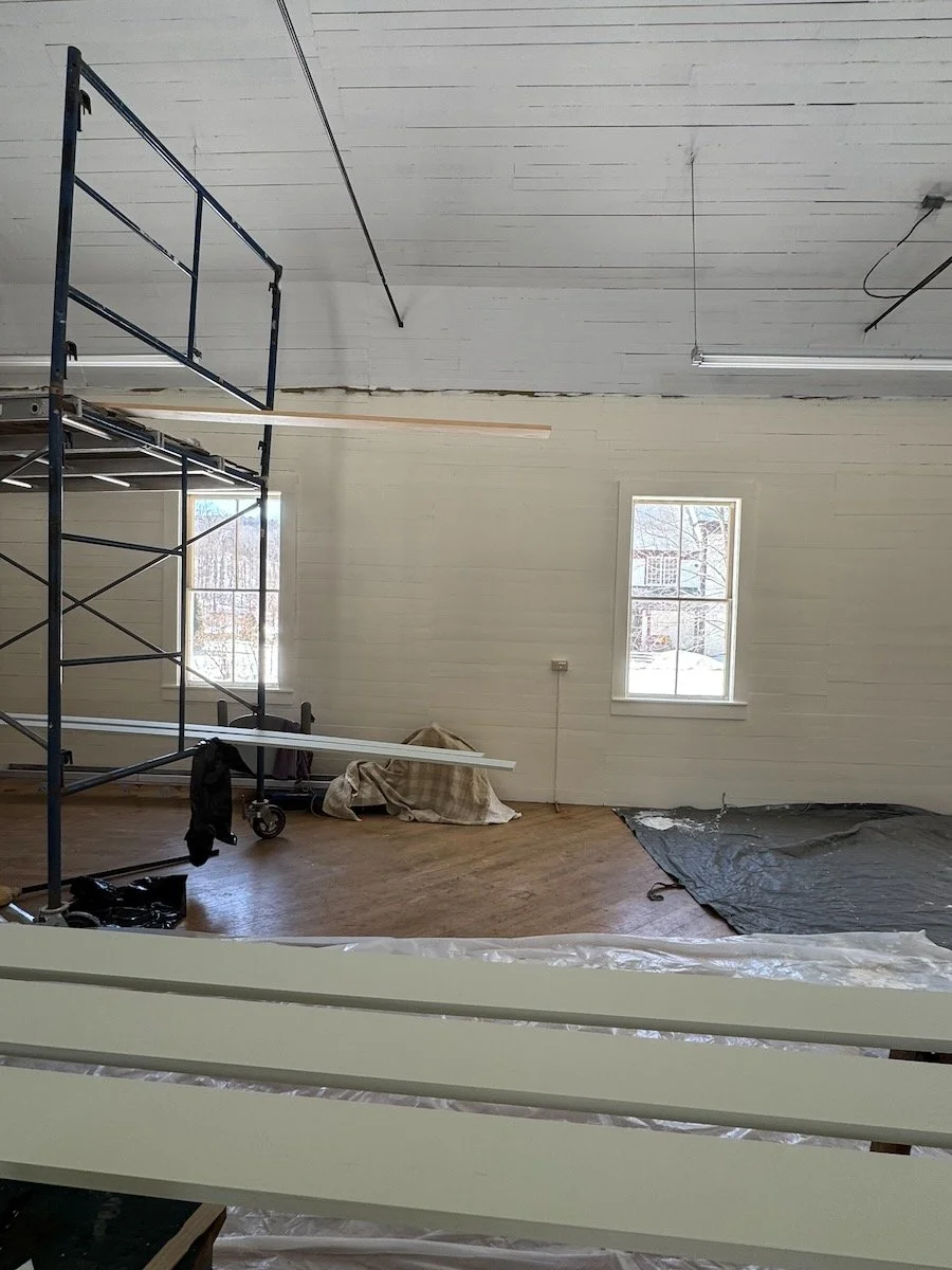 Interior room under renovation with scaffolding, windows, and construction materials including wood and plastic sheeting.
