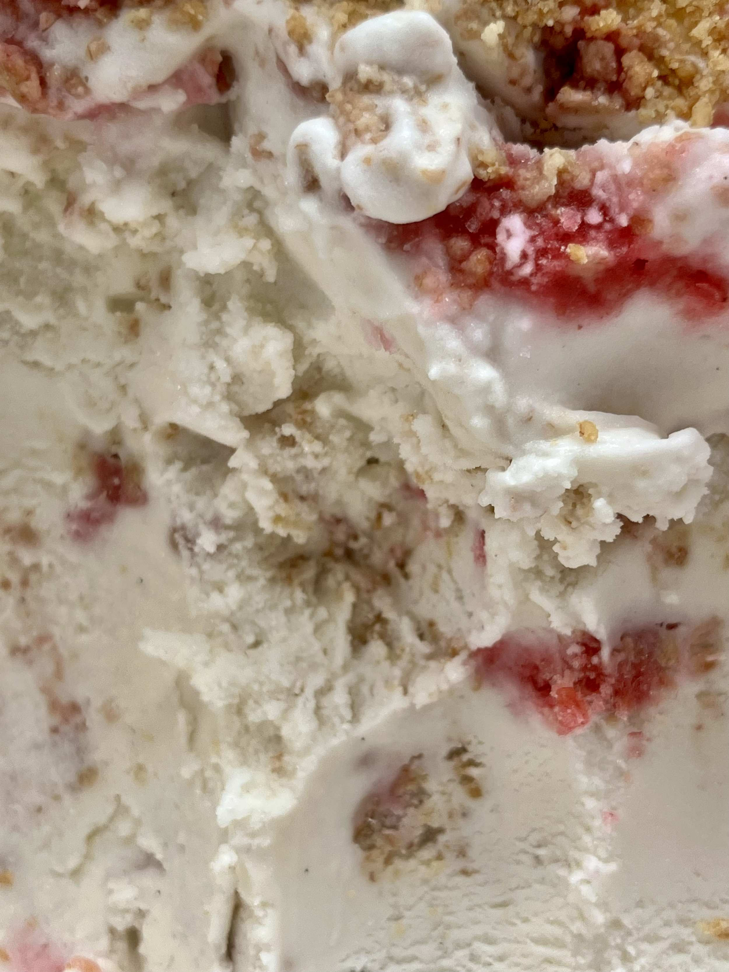 Close-up of coconut ice cream with swirls of raspberry ripple and digestive crumbs.