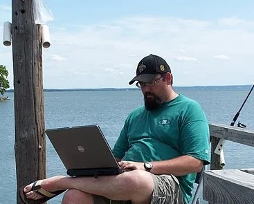 Travis Erwin sits on a fishing dock in the Texas HIll Country writing.