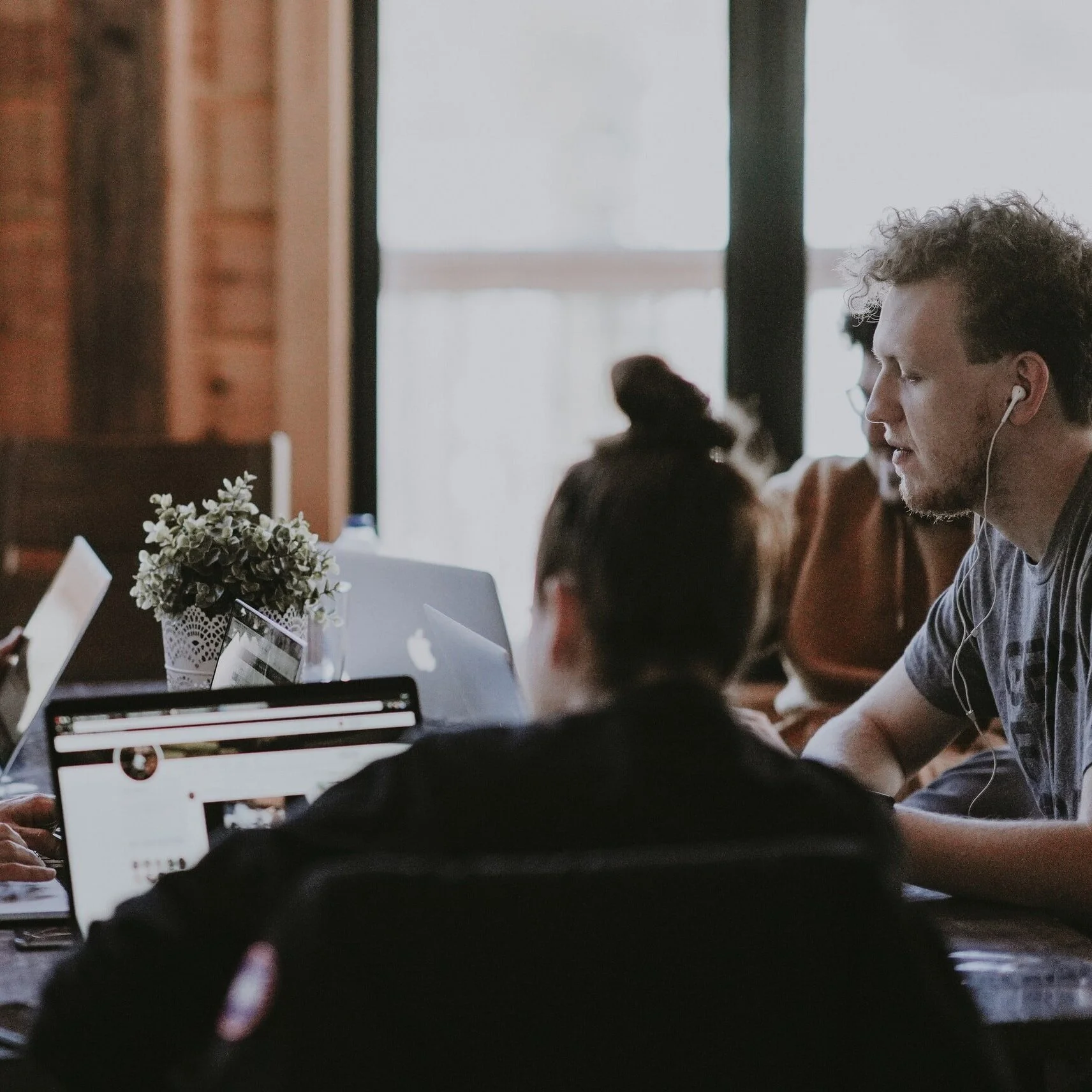 A woman in a burgundy blazer and black dress sitting on a bench, using a smartphone and a laptop.