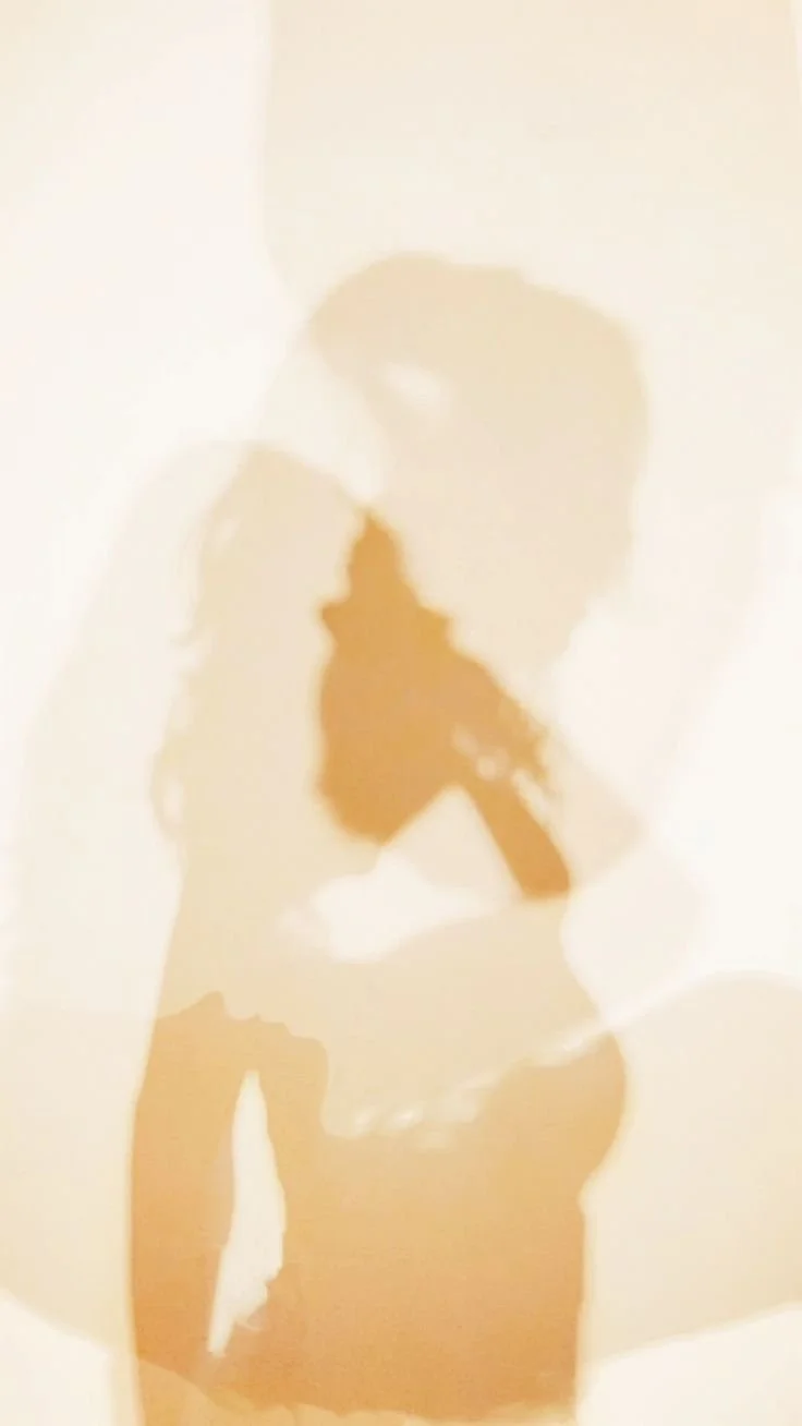Silhouette of a person holding a phone or camera, with their head turned, cast in warm light.