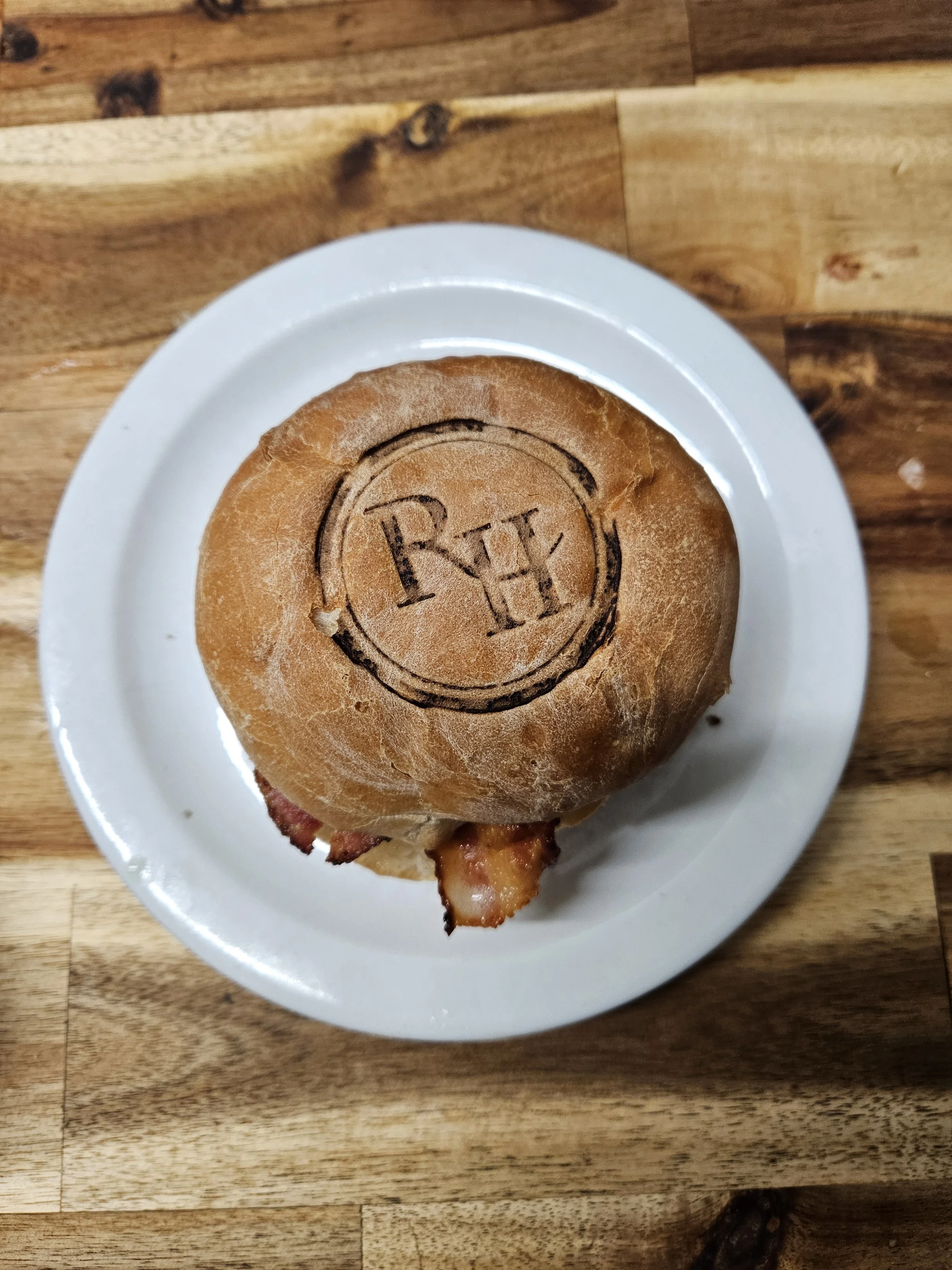 Bacon cheeseburger on a white plate atop a wooden table, with a cartoon face drawn on the bun.