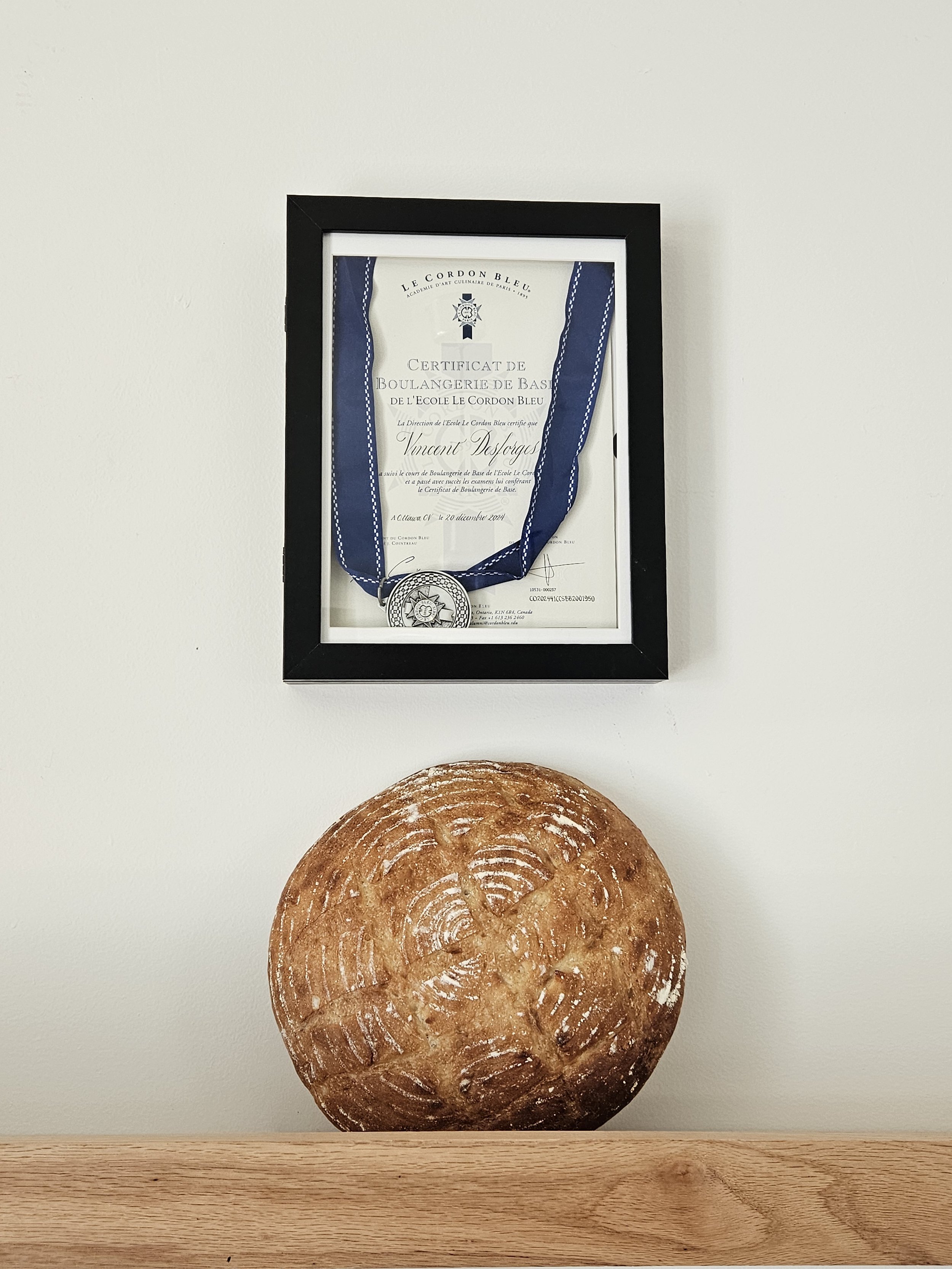 Framed Le Cordon Bleu basic bakery certificate with a blue-ribbon medal displayed above a rustic round loaf of bread.