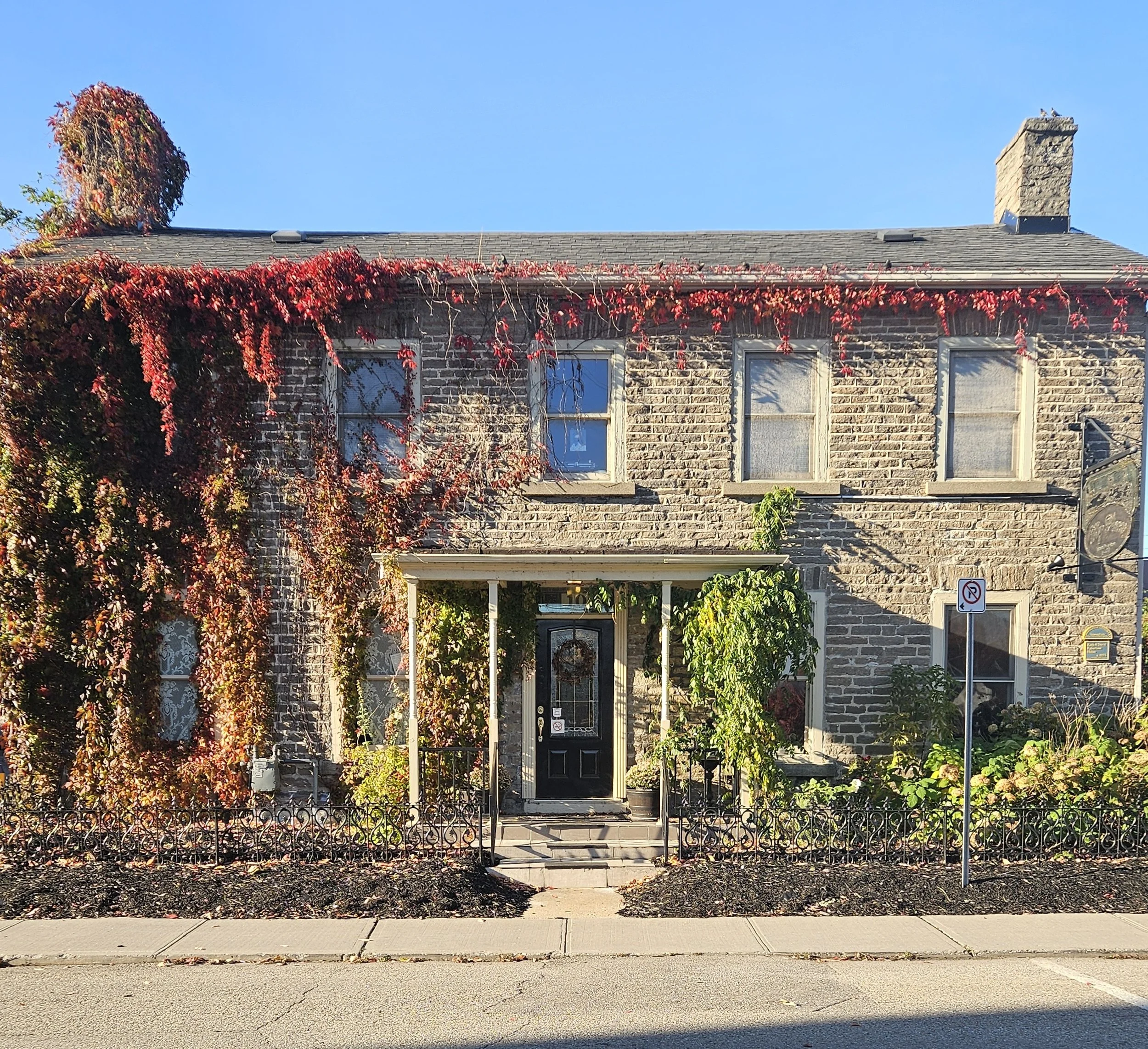 Historic stone townhouse with red autumn vines, black front door, covered porch, and garden fence