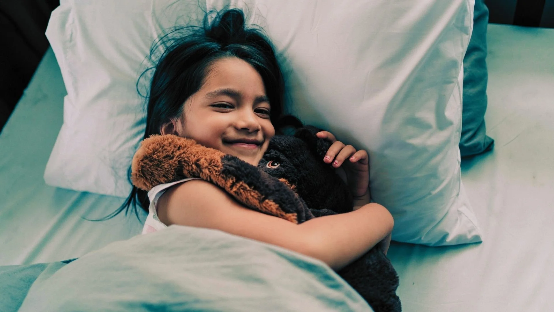 Méditation du soir pour accompagner les enfants vers un sommeil calme et paisible, illustrée par une petite fille souriante dans son lit avec son toutou.