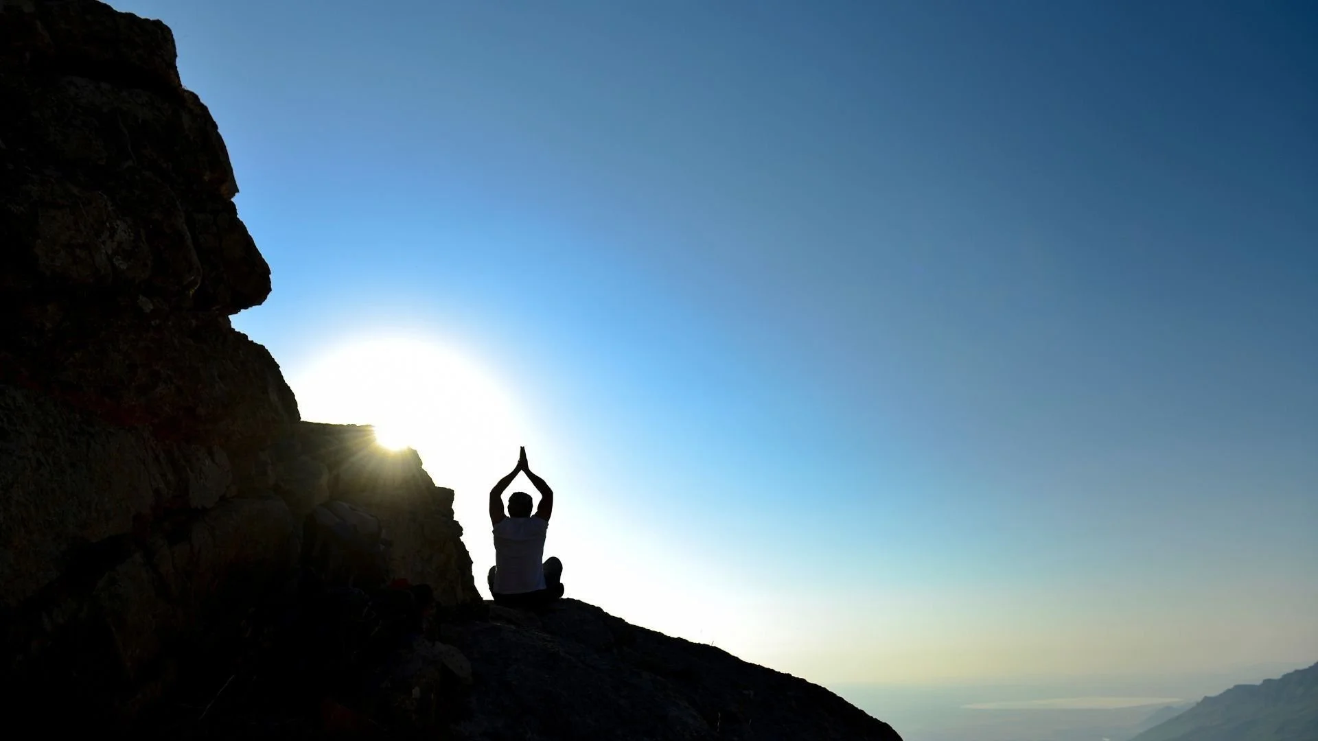 Personne assise les mains levées vers le ciel sur un sommet de montagne, sous un ciel bleu à perte de vue, illustrant la méditation Affirmation positive de Zen-toi pour ancrer le positif, nourrir l’estime de soi et renforcer l’alignement intérieur.