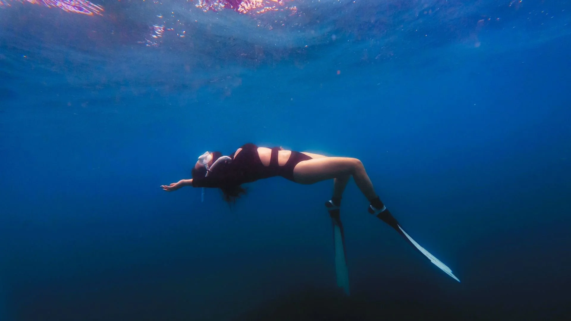 Femme en costume de bain prune et palmes, flottant sur le dos sous l’eau dans un océan bleu, portant un masque de plongée, illustrant la méditation Respiration cohérente de Respire Zen pour réguler la respiration et apaiser le système nerveux.