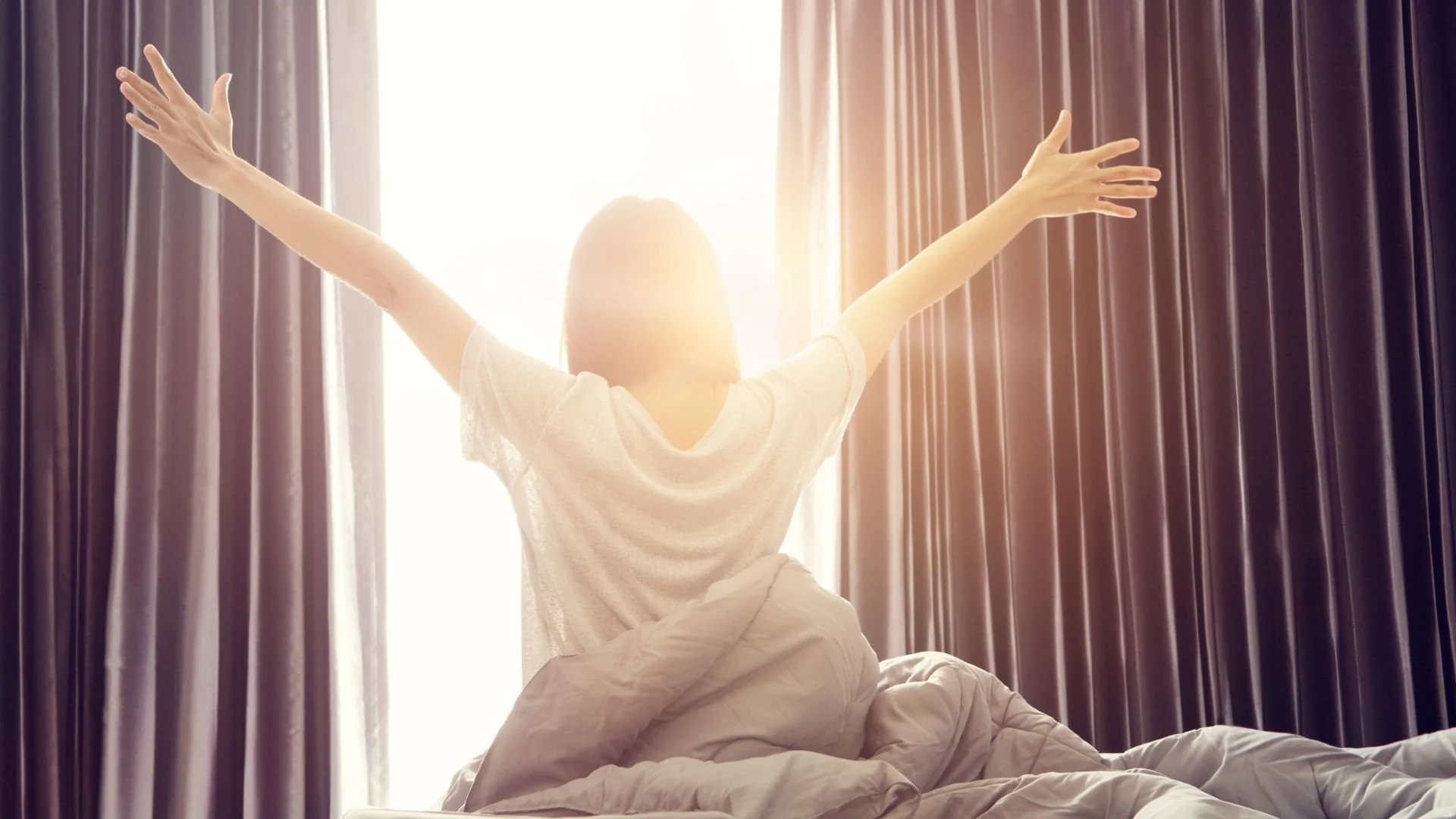 Femme en étirement sur son lit avec lumière du matin, illustrant une méditation de respiration pour le matin