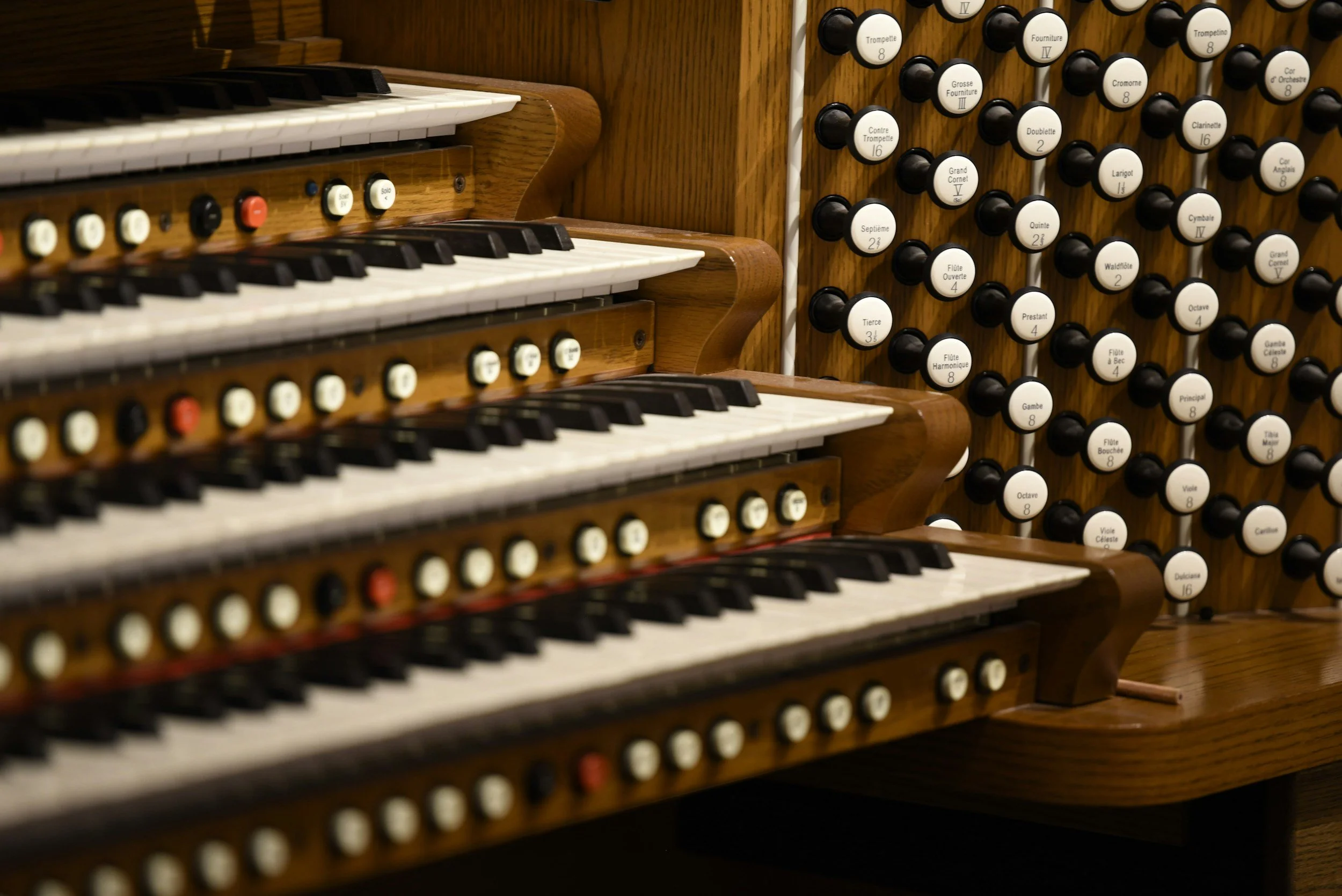 Close-up of a pipe organ with multiple rows of black and white keys and numerous labeled stops on a wooden panel.