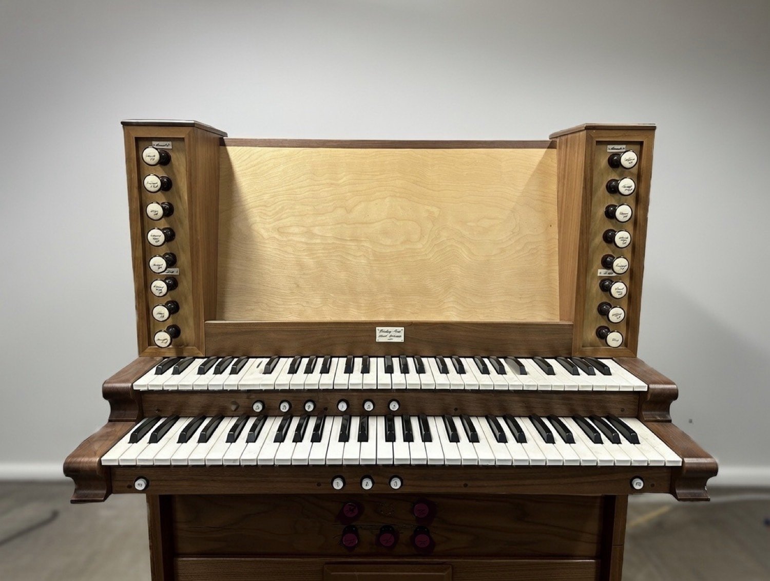 A vintage wooden pipe organ with black and white keys and multiple stops on each side.