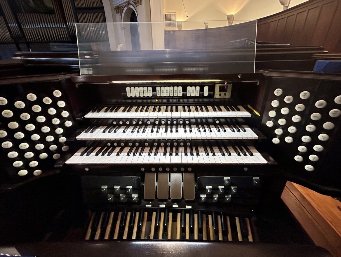 A pipe organ console with multiple manuals (keyboards), numerous stops on both sides, and various foot pedals.