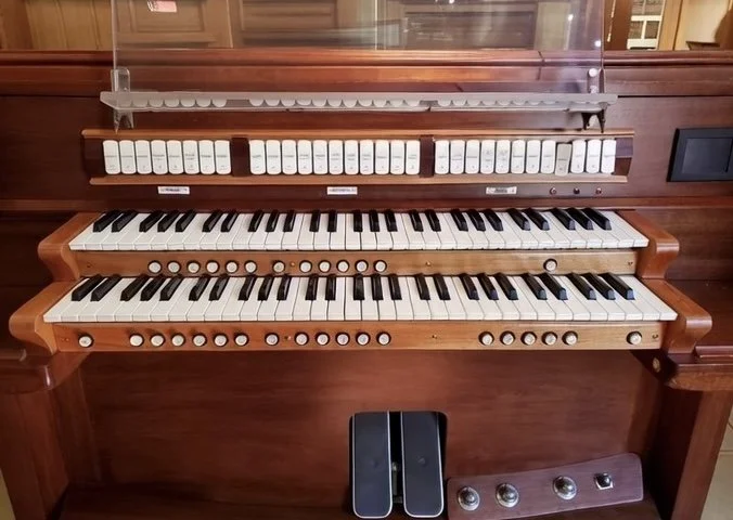 Close-up of a vintage upright pipe organ with multiple manuals and stops, showing three keyboard manuals and a row of numbered stop tabs.
