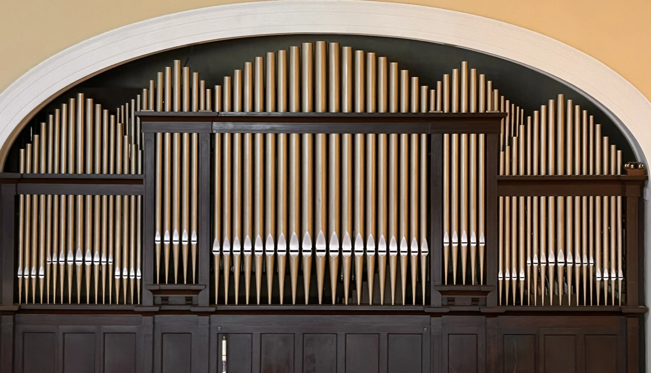 A large pipe organ with wooden pipes of varying heights arranged in a symmetrical pattern with a dark wooden frame and an arched top.