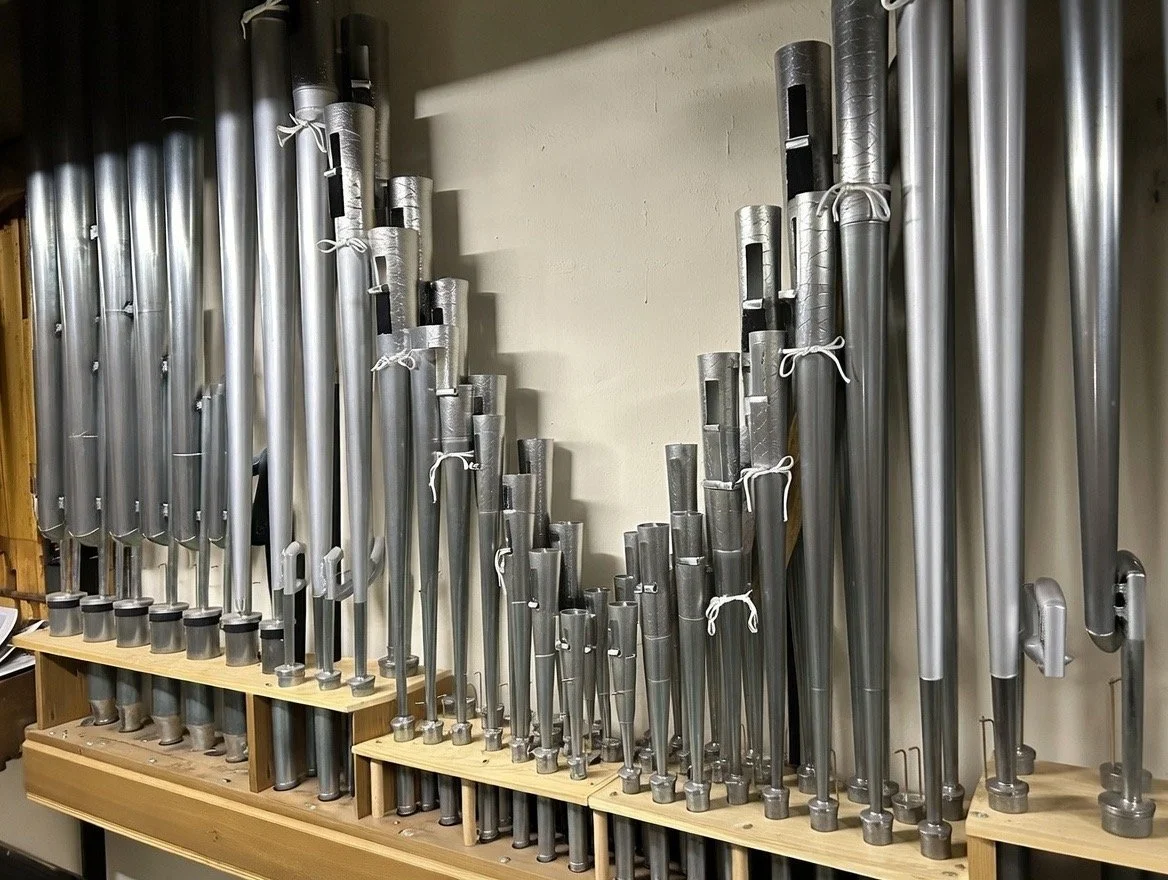 A display of various metal pipes, some tied with white strings, on a wooden shelf against a plain wall.