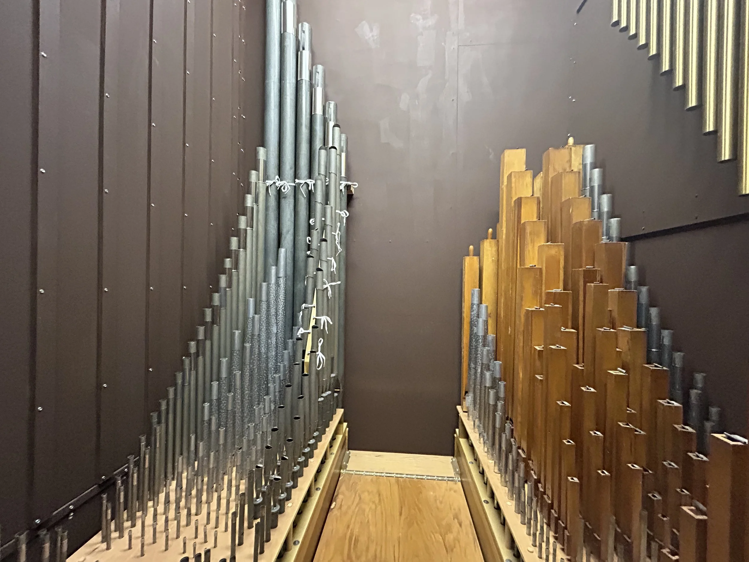 Two large organ pipes, one on the left and one on the right, mounted on wooden bases against a dark wall.