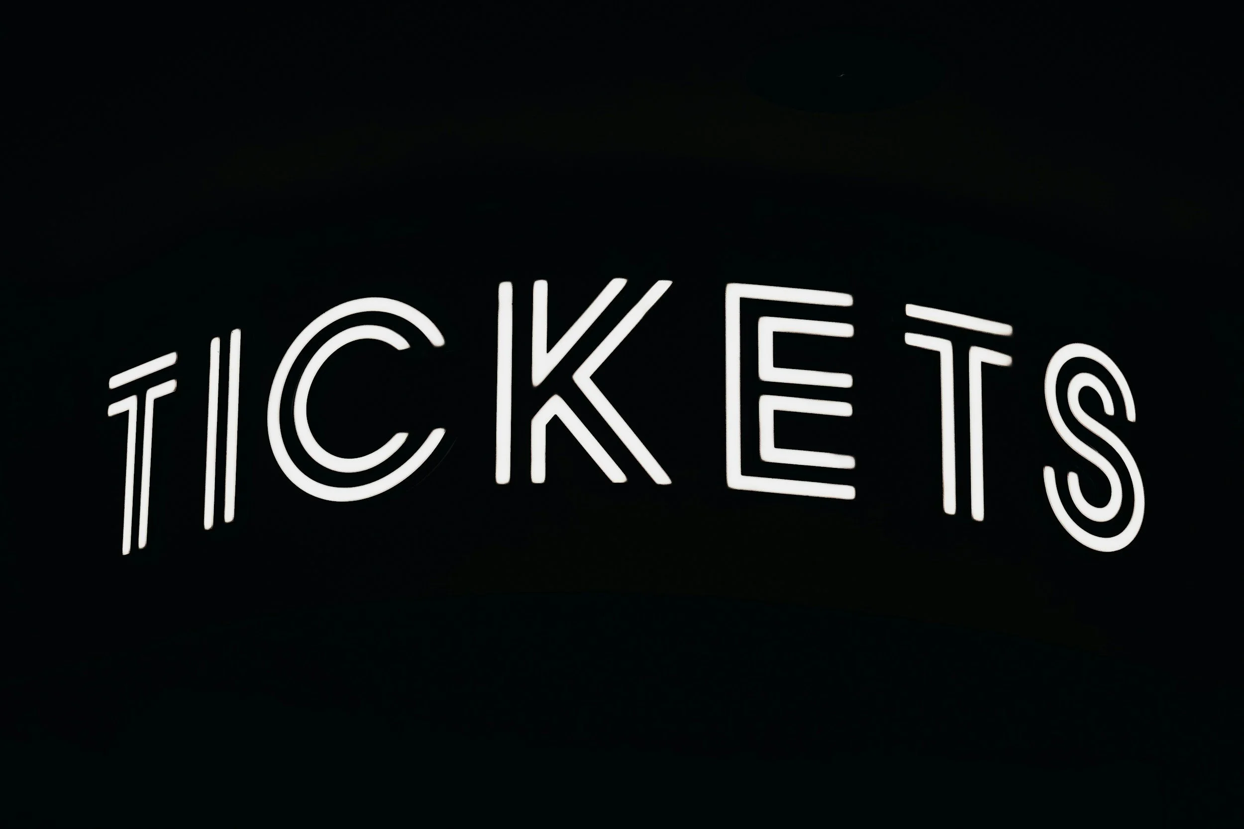 Neon sign spelling out the word 'TICKETS' against a dark background.