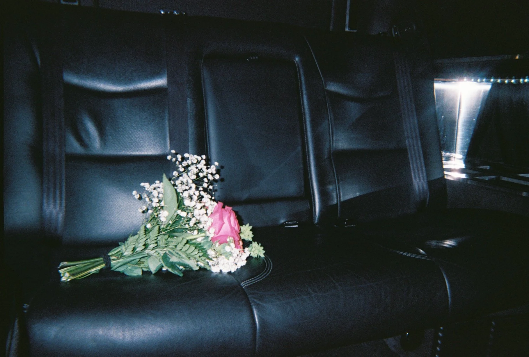 A bouquet of pink and white flowers resting on a black leather car seat.