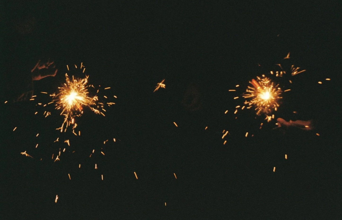 Two sparkler fireworks burning on a dark night, emitting bright sparks.