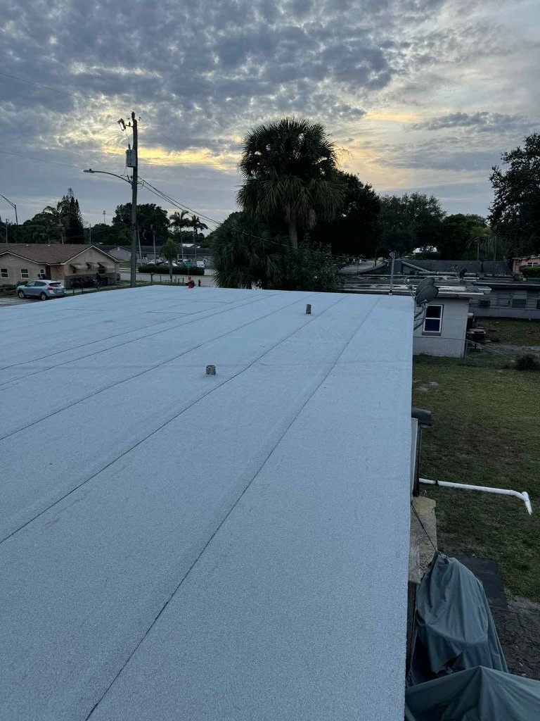 View of a residential roof with a white surface, a satellite dish, and a nearby electrical pole with wires against a cloudy sky at sunset.